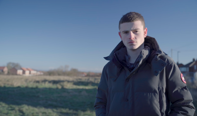 A young man looking into a camera with a blue sky behind him