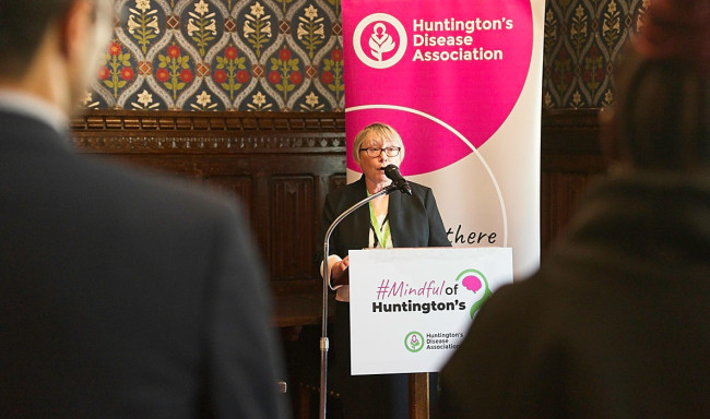 Image of a woman with blonde hair stood in front of a microphone with a banner behind her