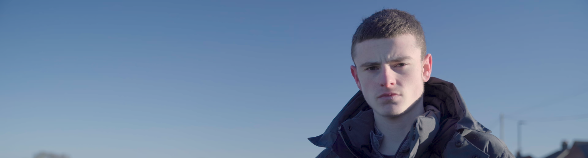 A young man looking into a camera with a blue sky behind him