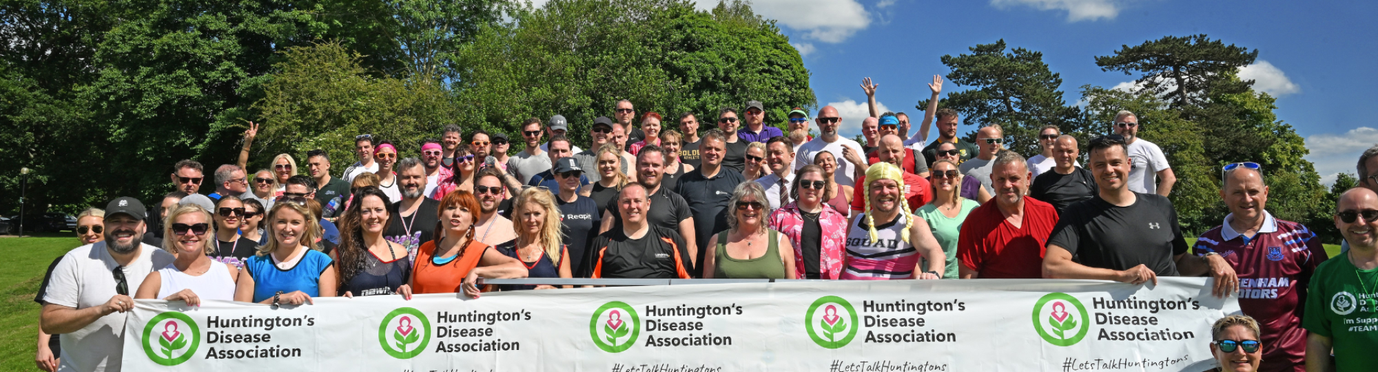A group of enthusiastic fundraisers standing in a field with a sign saying Do it for Dom 2024