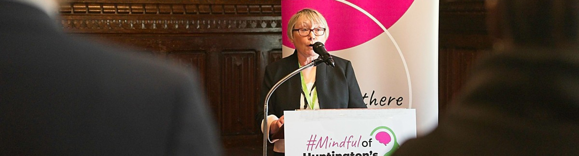 Image of a woman with blonde hair stood in front of a microphone with a banner behind her
