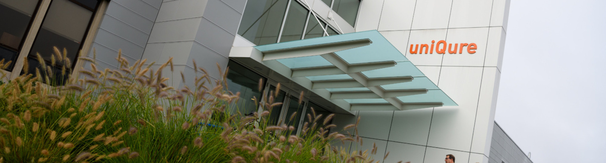This is a picture of uniQure building with the sign visible and people walking up to the entrance